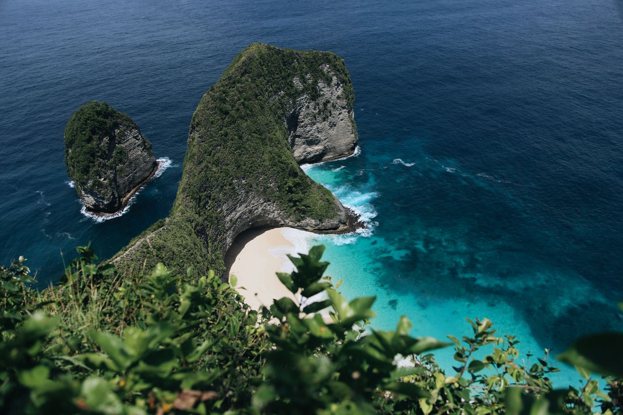 Stunning aerial view of Nusa Penidas picturesque beach in Bali surrounded by clear turquoise waters and lush green cliffs.